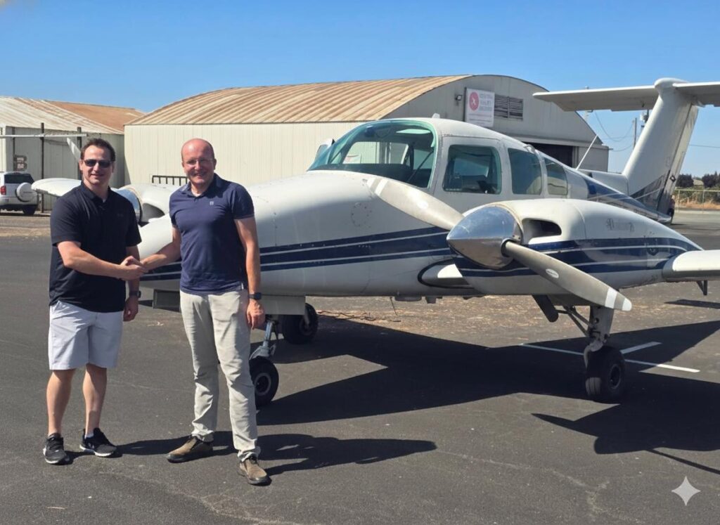 Two MEIs stand on an airport tarmac, shaking hands and smiling in front of a small twin-engine airplane—celebrating the MEI benefits and answering "do I need MEI" under a clear blue sky, with a large hangar visible in the background. - CFI Academy