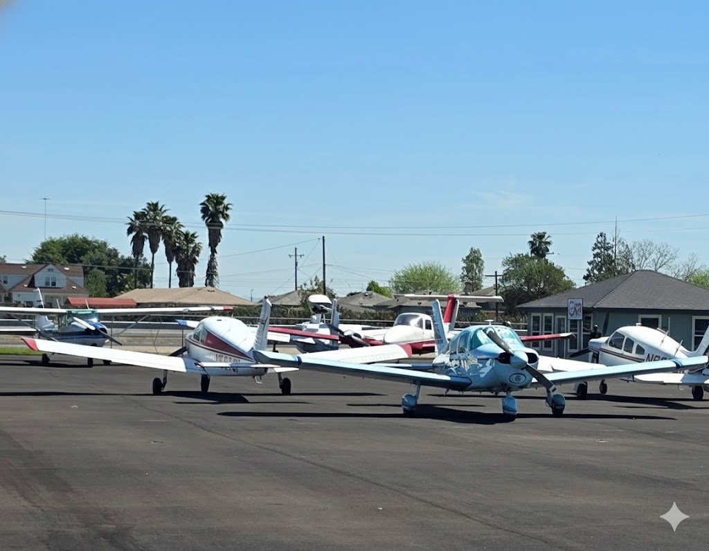 Several small propeller planes are parked on an airport tarmac under a clear blue sky, with palm trees, buildings, and a fence in the background. - CFI Academy