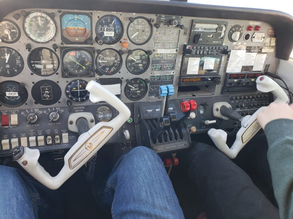 Two people sit in the cockpit of a small aircraft, each holding a yoke. The panel is filled with gauges and controls. Both are wearing jeans, likely engaged in CFI training California as they practice procedures together. - CFI Academy
