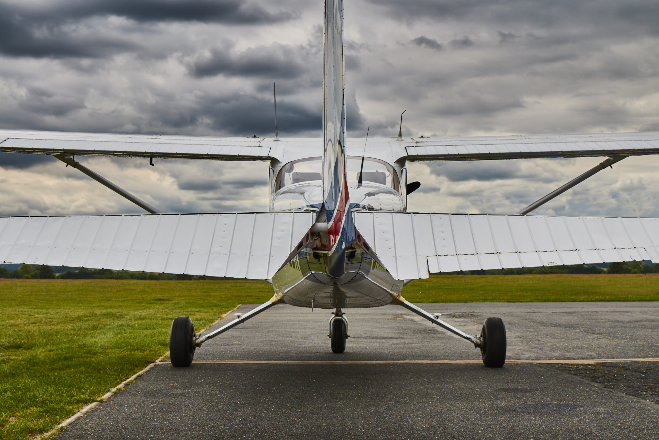 A small single-engine airplane viewed from behind, parked on a runway with green grass on both sides under a cloudy sky—an ideal setting for CFI training California, where pilot training policies and weather cancellations are top of mind. - CFI Academy